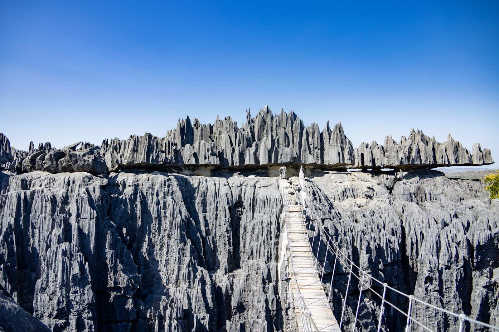 The suspension bridge of the Great Tsingy de Bemaraha spanning a canyon of grey limestone blades under a blue sky