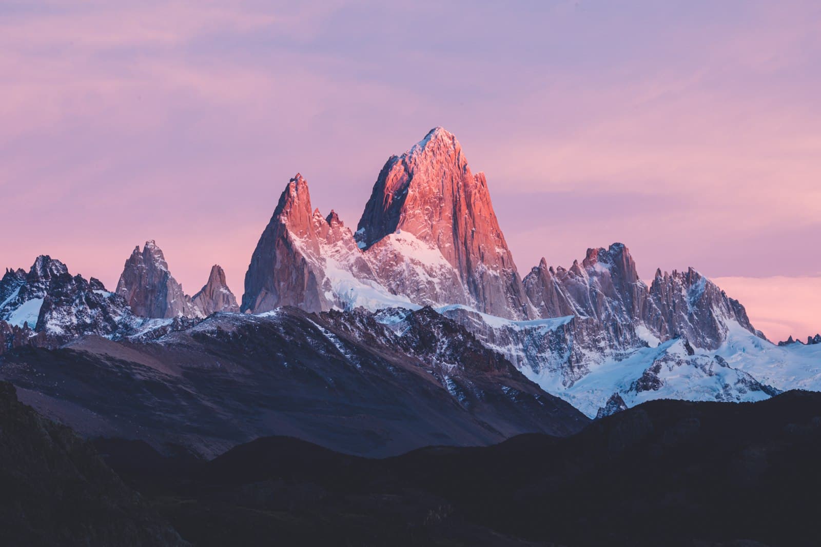 The Fitz Roy massif and its snow-dusted granite needles glowing pink at sunrise, above the dark ridges of Patagonia