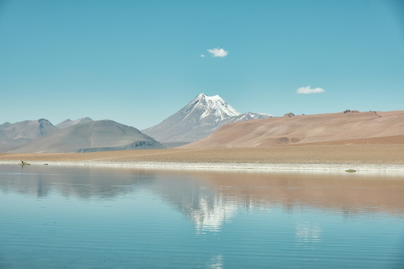 A snow-capped volcano reflected in the still water of a high-altitude lagoon in the Atacama desert
