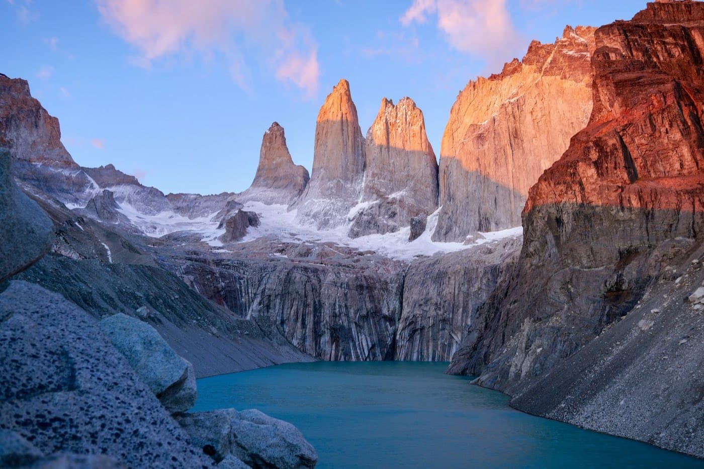 The three granite towers of Torres del Paine lit by sunrise above the turquoise glacial lagoon