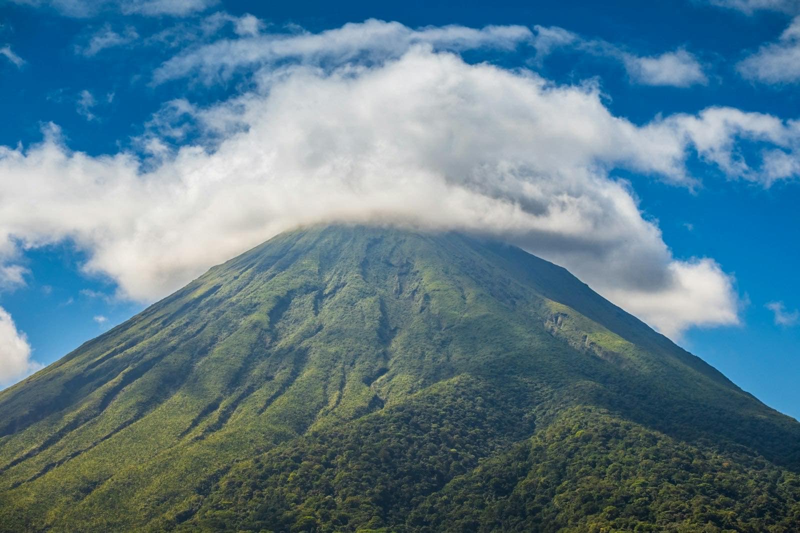 Le cône parfait du volcan Arenal coiffé d'un nuage, couvert de forêt tropicale