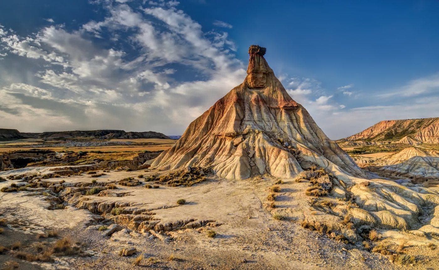 The Castildetierra fairy chimney rising above the ochre badlands of the Bardenas Reales, beneath a blue sky streaked with clouds