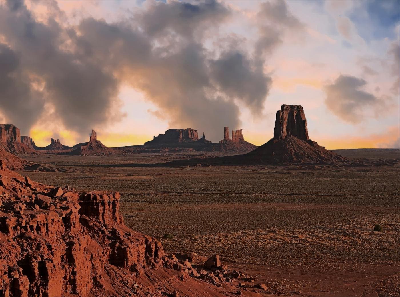 The red buttes of Monument Valley under a sunset sky, ochre desert in the foreground