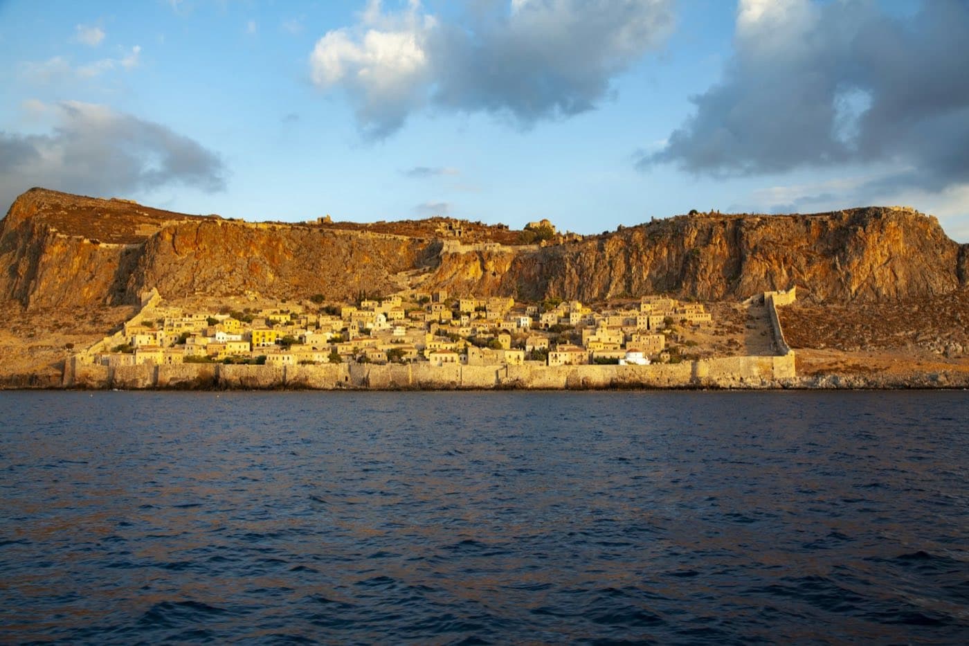 La ville basse fortifiée de Monemvasia blottie sous son rocher, vue depuis la mer dans la lumière dorée du soir