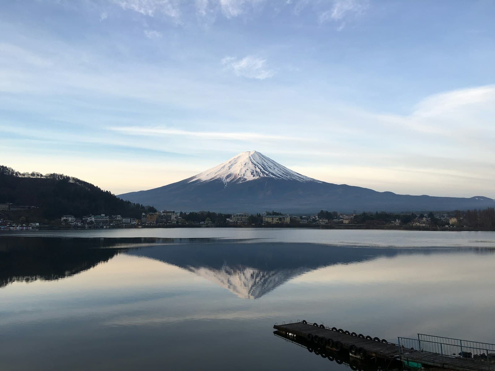 Snow-capped Mount Fuji reflected in the calm waters of Lake Kawaguchi at sunrise, a pontoon in the foreground