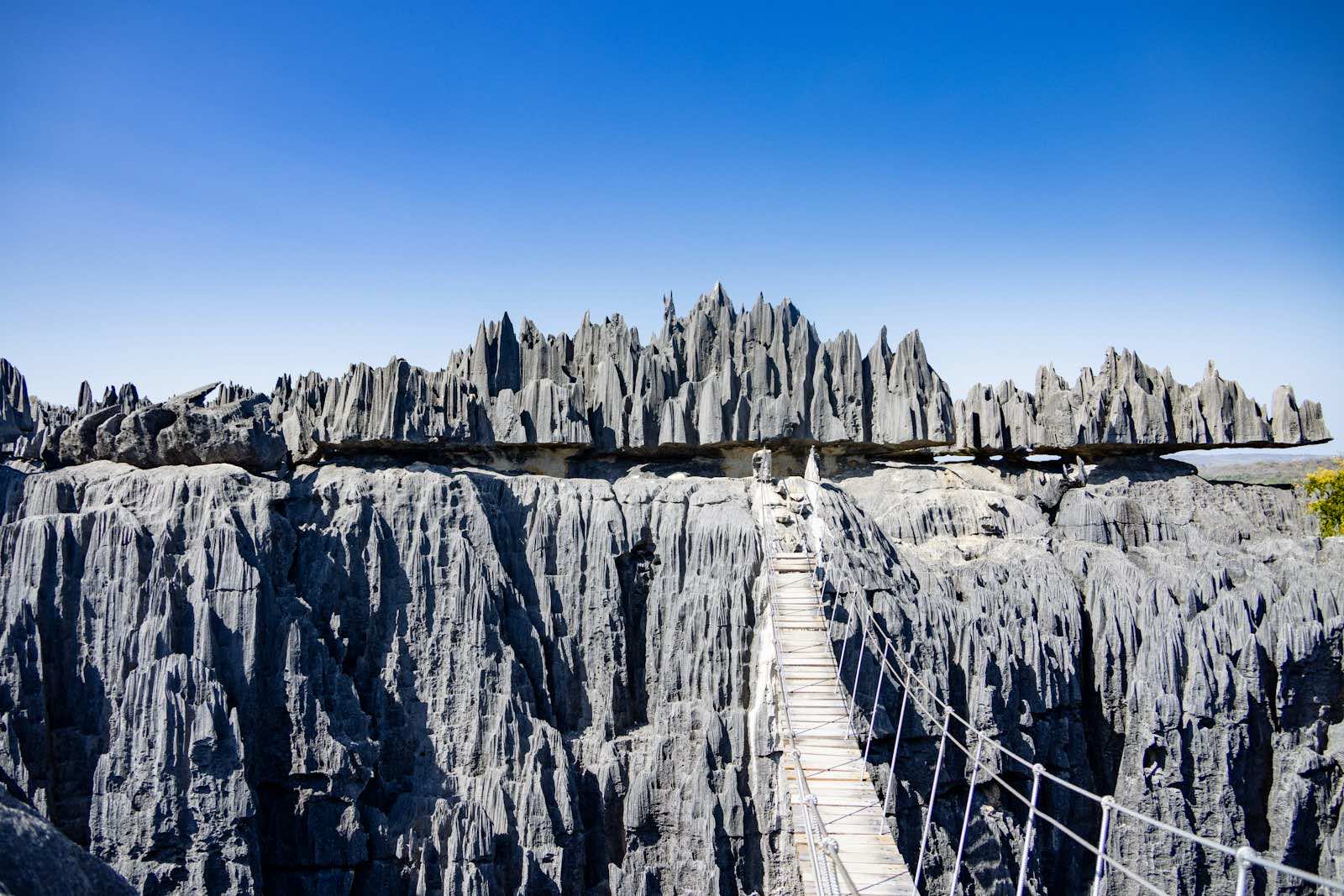 The suspension bridge of the Great Tsingy de Bemaraha spanning a canyon of grey limestone blades under a blue sky