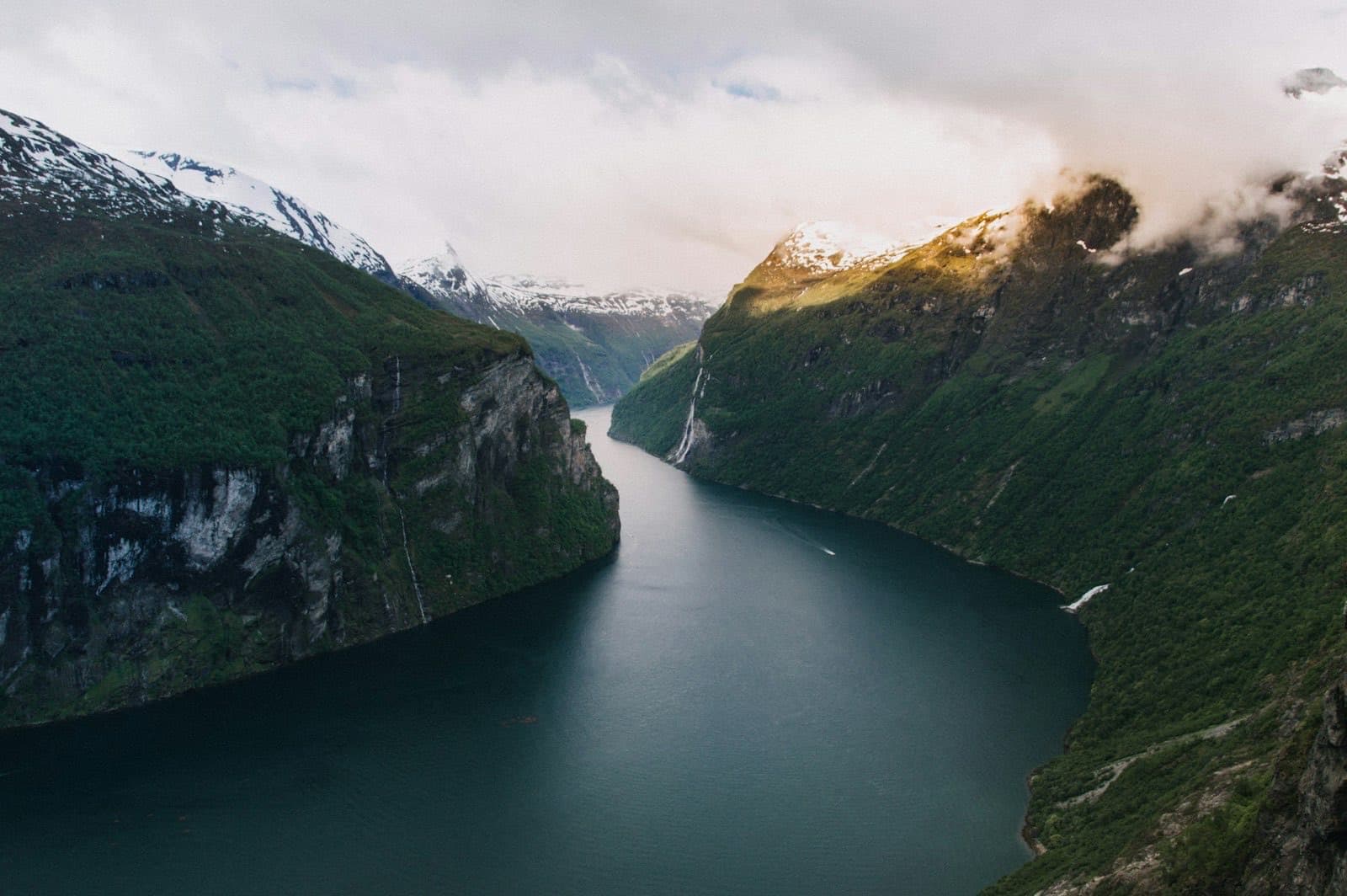 Le Geirangerfjord vu d'en haut, parois vertes et sommets enneigés, avec la cascade des Sept Sœurs tombant dans le fjord
