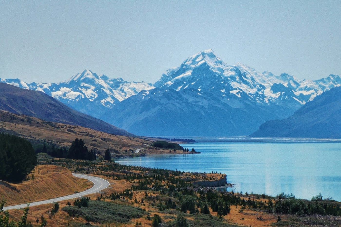The SH80 road winding along turquoise Lake Pukaki towards snow-capped Aoraki/Mount Cook