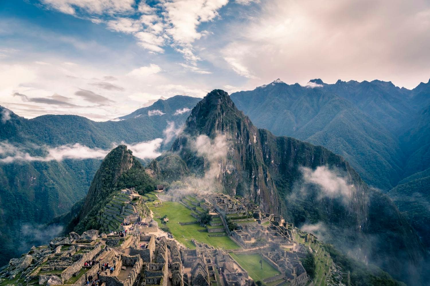 The Inca citadel of Machu Picchu and its green terraces before the Huayna Picchu peak, with clouds clinging to the mountains