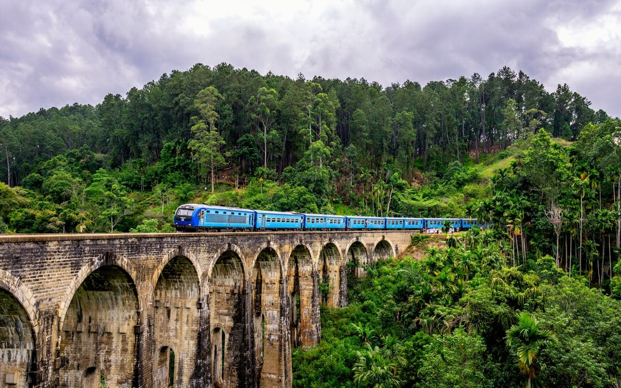 A blue Sri Lankan train crossing the brick Nine Arch Bridge viaduct amid the forest near Ella